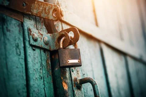 An old rusty lock hangs on the abandoned wooden gate, painted blue, which clo Stock Photos