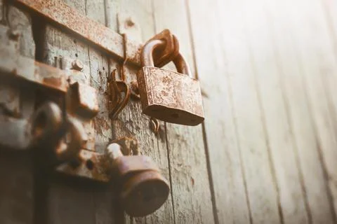An old rusty lock hangs on the old painted gate, closing it, illuminated by s Stock Photos