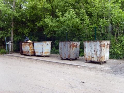 Old rusty metal garbage dumpsters standing along a roadside near a green fo.. Stock Photos