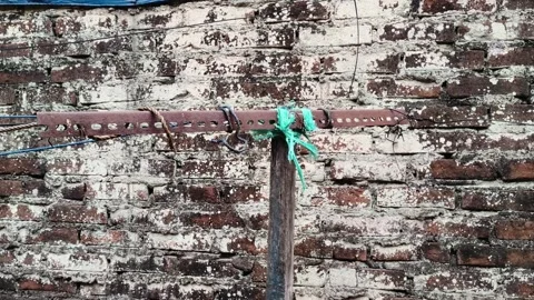 Old rusty metal pole with clothesline in front of weathered brick wall 库存影片 347693093