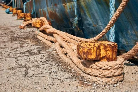 Old rusty mooring bollards and thick hemp ropes securing a large ship in a .. Stock Photos