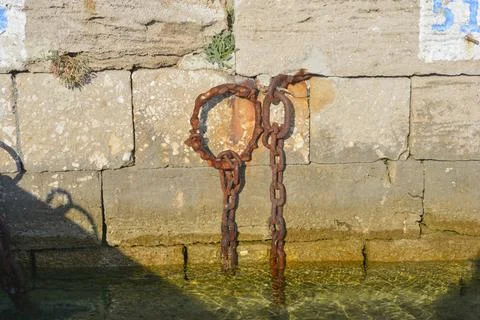 Old rusty mooring chains hanging on stone dock wall Stock Photos