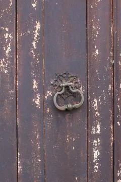 Old rusty openwork wrought iron ring on a wooden door made of wood with peeling Stock Photos