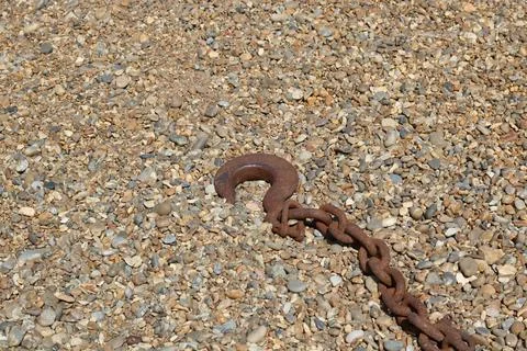 Old rusty orange brown nautical chain with hook lying on shingle beach Stock Photos