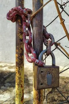 An old, rusty padlock with a chain hanging from the gate Stock Photos