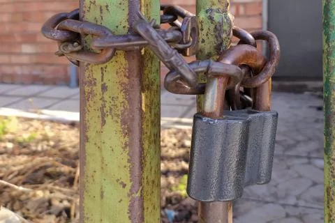 An old, rusty padlock with a chain hanging from the gate Stock Photos
