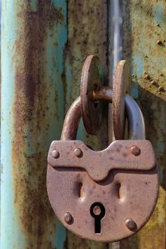 An old, rusty padlock with a chain hanging from the gate Stock Photos