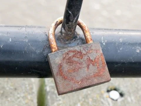 Old rusty padlock up close locked on black metal gate Stock Photos