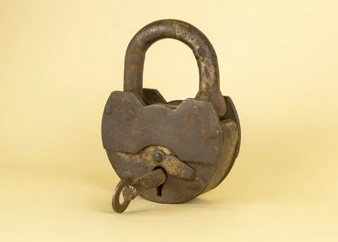 An old rusty padlock with a key in the middle on a beige background. Stock Photos
