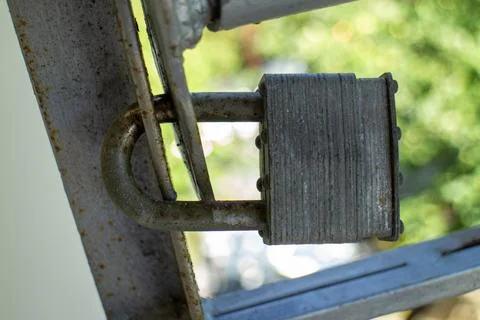 Old rusty padlock securing a metal gate outdoor with a blurred green background 库存照片