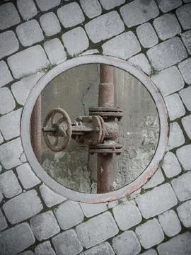 An old rusty pipe at the bottom of an open sewer manhole on the sidewalk. Stock Photos