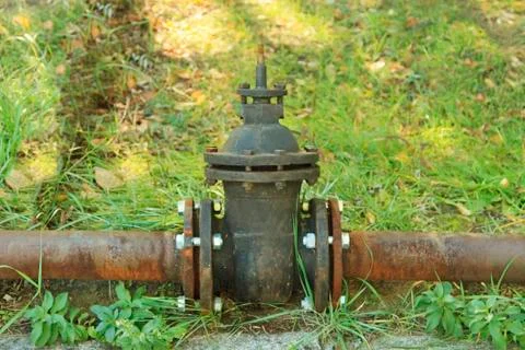 Old rusty pipe with shut-off valve over green grass Stock Photos