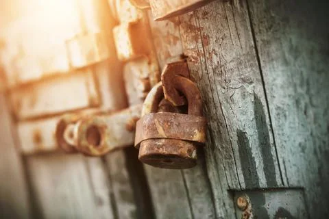 An old rusty retro padlock hangs on an old wooden gate, painted with blue pai Stock Photos
