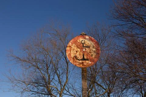 Old rusty round do not moor sign with an anchor in front of winter tree branches Stock Photos