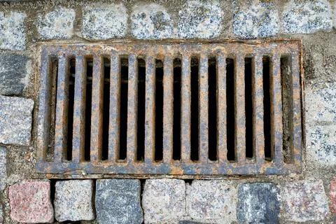 An old rusty sewer grate in a stone pavement on a city street. Stock Photos