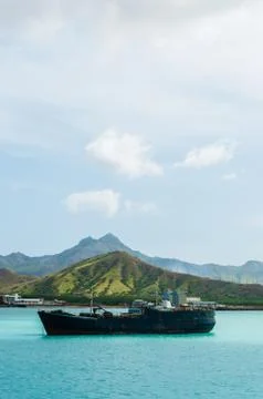 Old rusty Ship in the blue ocean at coast with cloud and green mountain Stock Photos
