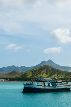 Old rusty Ship in the blue ocean at coast with cloud and green mountain Stock Photos
