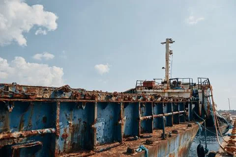 Old rusty shipwreck abandoned and docked at a port terminal under a blue sky Stock Photos