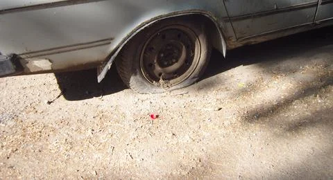 Old rusty silver car with a completely flat rear tire, parked on a dusty, d.. Stock Photos