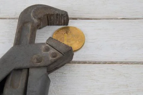 Old rusty silver pipe spanner clamps a golden coin bitcoin Stock Photos