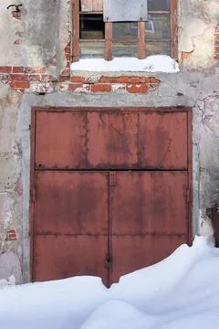 An old rusty snow-covered gate in the wall of an abandoned industrial buildin Stock Photos