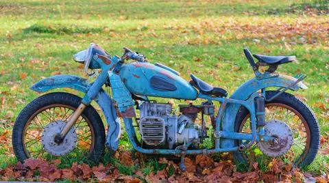 Old rusty soviet motorcycle in blue standing on a background of green grass a Stock Photos