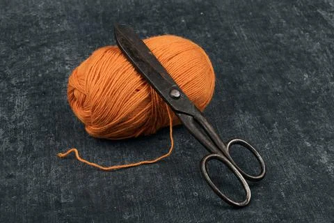 Old rusty tailor scissors and a tangle of orange color woolen yarn in close-u Stock Photos