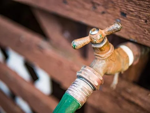 Old rusty water faucet and hose on a wooden house Stock Photos