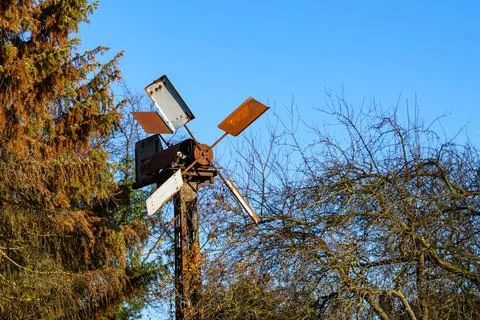 Old rusty windmill among the trees. Autumn sunny day and clear blue sky. Stock Photos