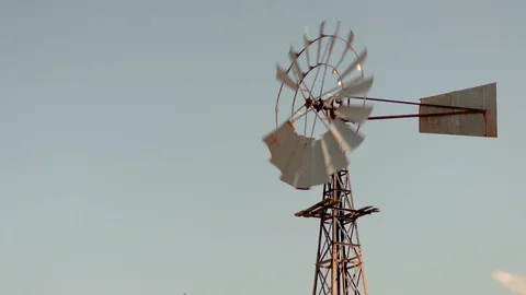 Old Rusty Windmill turning in the wind on a dry farm at golden hour. Stock Footage