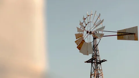 Old Rusty Windmill turning in the wind on a dry farm at golden hour. Video stock 94401573