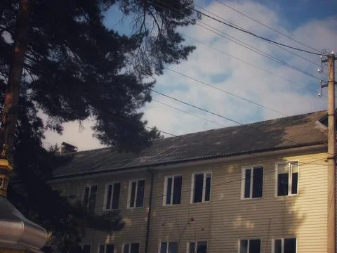 Old sanatorium building behind pine trees under sunny blue sky Stock Photos