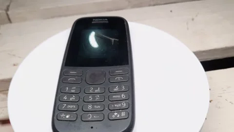 Old school cellphone displayed on white rotating display, black cellphone wit Stock Footage 255519316