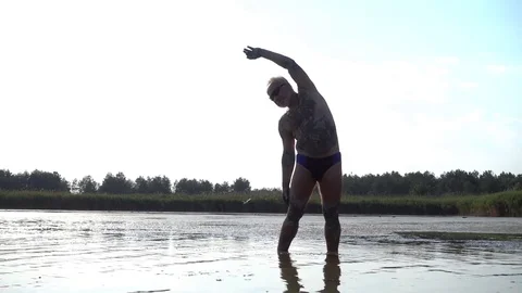 An old senior Man do Gymnastics standing in the Lake Water, rubbed with Clay Mud Stock Footage