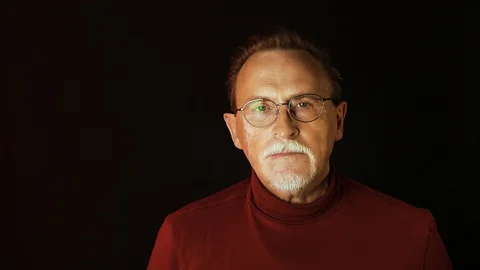 Old senior man man in glasses looking at camera on dark background. Stock Footage 129181005