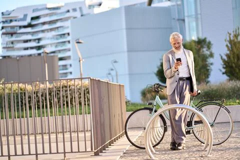Old senior man using phone using bike rental app renting bicycle in city park. Stock Photos