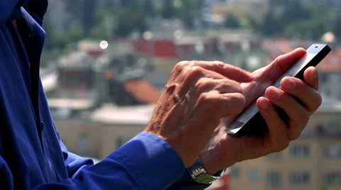 Old senior man works (typing) on smartphone - city (buildings) in background Stock Footage