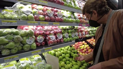 Old senior woman picking using a black N95 face mask and  jacket choosing pears Stock Footage 150448638
