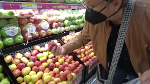 Old senior woman picking using a black N95 face mask and jacket choosing apples Stock Footage 150448646