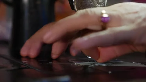 An old sewing machine runs as hands guide a torn black bag under the needle with Stock Footage 312108926