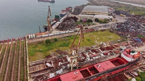 Old ship is docked at a busy port with cranes and scrap yard nearby Stock Footage 338324500