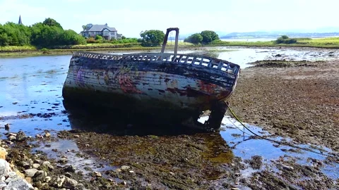 An old ship lies in the shallow water of the ocean at low tide Ireland Stock Footage 230166384