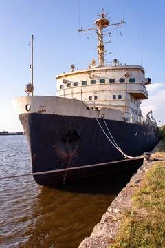 Old ship rests at water's edge, weathered and silent. Bare hull shows signs o Stock Photos