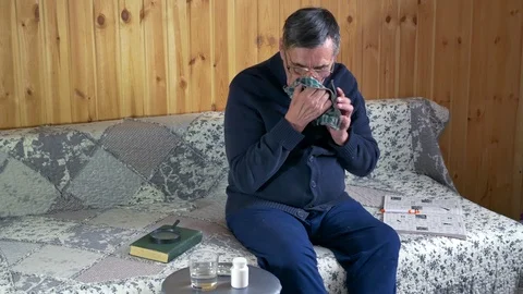 Old sick man sitting on the sofa has a runny nose uses handkerchief Stock Footage