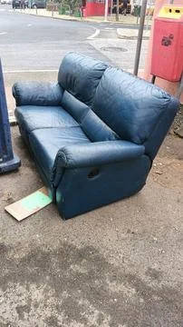 An old skin sofa was thrown into a landfill next to a garbage can on one of the Foto stock