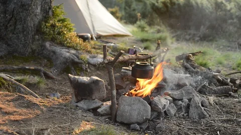 Old small kettle is heated on a bright bonfire on a green mountain meadow Stock Footage 95681376