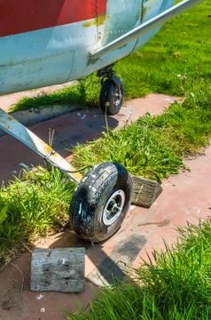 Old small single engine airplane wheel and wooden chocks on parking pad. Stock Photos