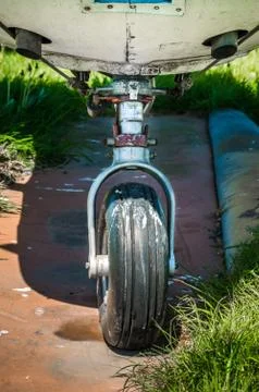 Old small single engine airplane landing gear on grassy overgrown parking pad. Stock Photos