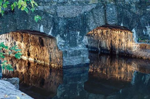 Old, small stone bridge close-up across small river, warm sunlight reflected  Stock Photos
