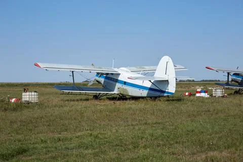An old Soviet plane white with a blue stripe is standing in a field at the ai Stock Photos